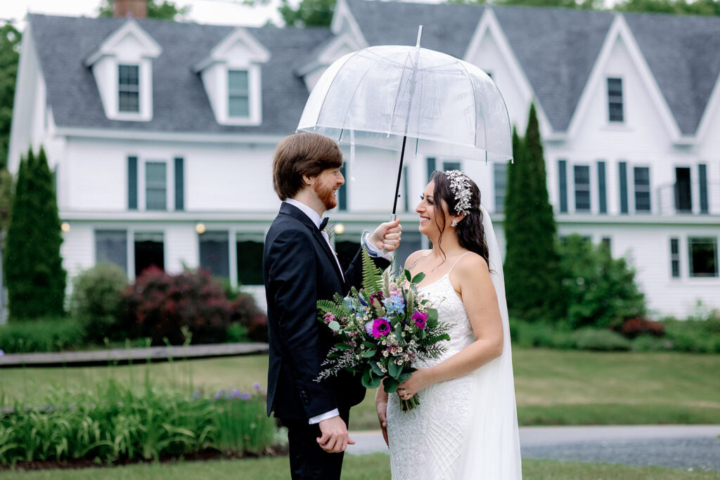 Bride and groom holding an umbrella in front of the Inn at Pleasant Lake