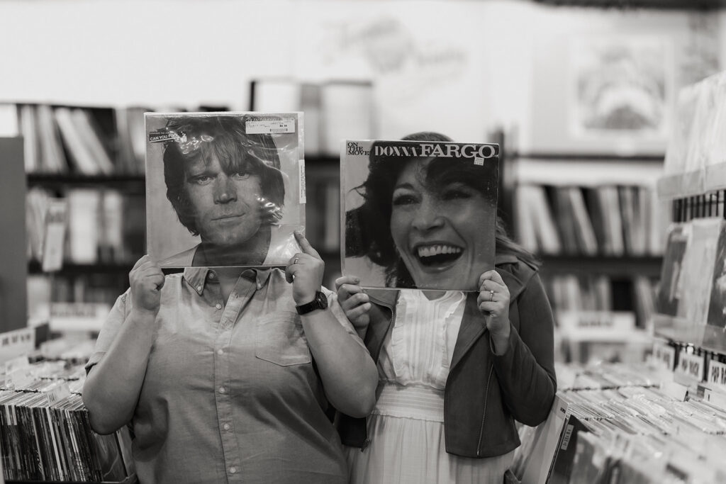 Two people holding up records in a record store.