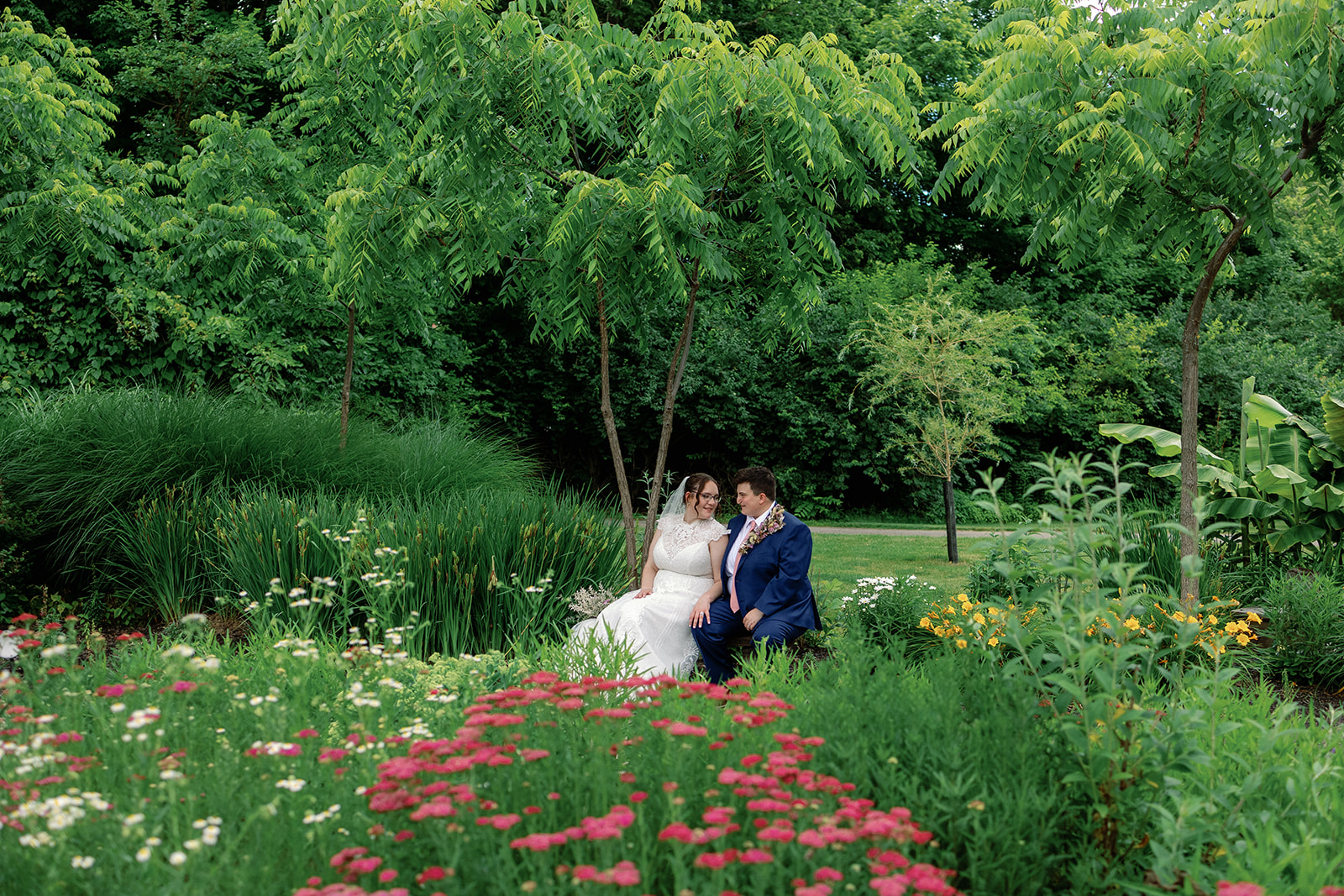 Two brides sitting on a bench in a colorful garden.